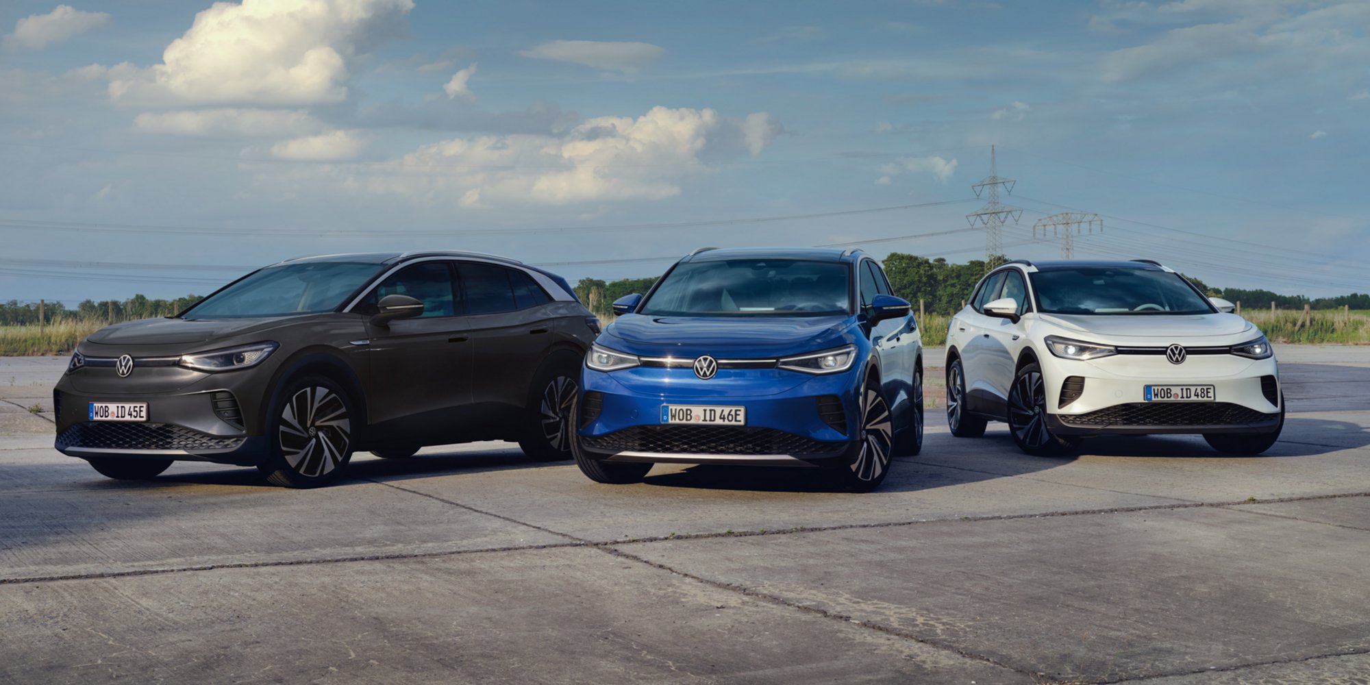 Drei VW ID.4 Elektroautos in Schwarz, Blau und Weiß stehen nebeneinander auf einer Betonfläche im Freien.