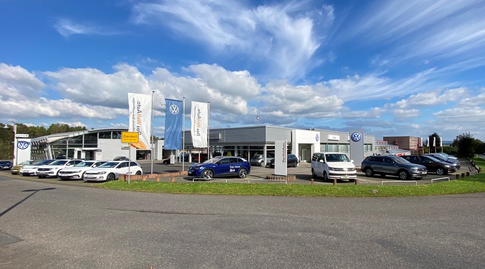 Autohaus mit mehreren Fahrzeugen vor dem Gebäude und Fahnen wehen im Vordergrund.