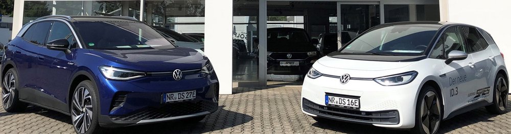 Das Bild zeigt zwei Volkswagen-Elektroautos, ein blaues und ein weißes, vor einem Autohaus.